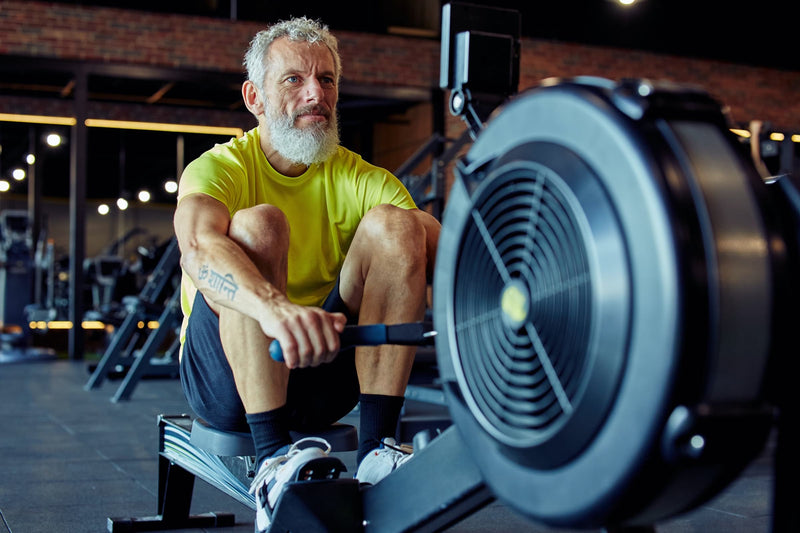 A older gentleman working out on a rowing machine at a gym.